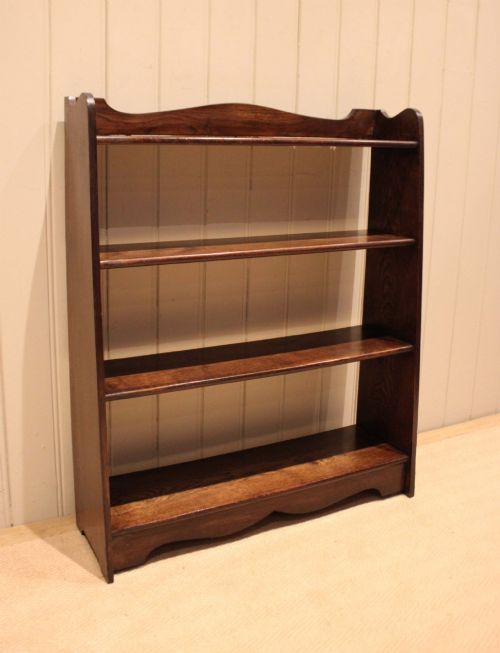 fig 1. A dark oak open bookcase with three shelves filled with books, featuring a gently curved top cresting and shaped apron.