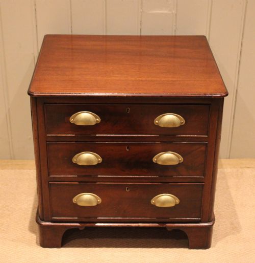 fig 1. A mid-19th century small low mahogany chest of drawers featuring three graduated drawers with brass cup handles and bracket feet.