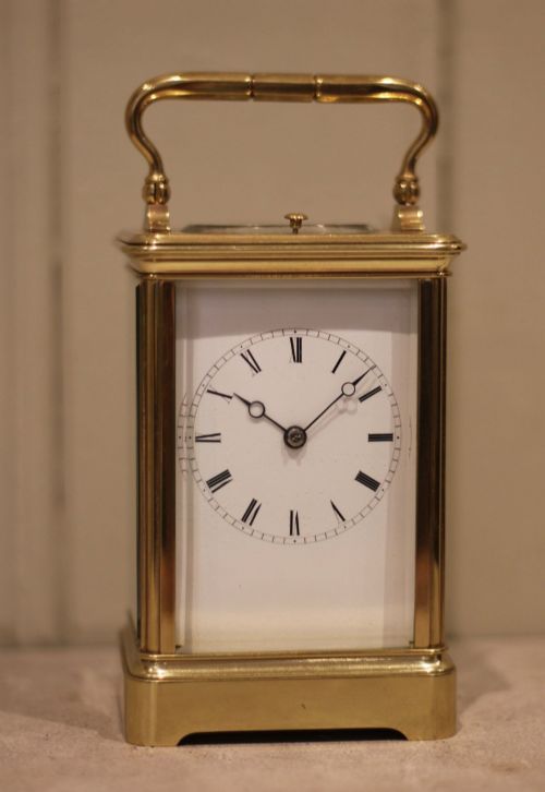 fig 1. A nineteenth-century French polished brass carriage clock featuring bevelled glass side panels, a white enamel dial with Roman numerals, and a hinged top carrying handle.