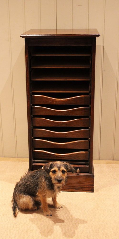 A tall dark oak single-column filing cabinet featuring a slatted wooden tambour front with top brass pull knobs and a keyhole escutcheon. View XI
