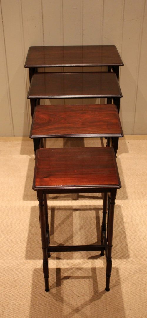A set of four graduated mahogany nesting tables featuring rectangular tops with moulded edges, slender turned legs, and connecting stretchers. View VI