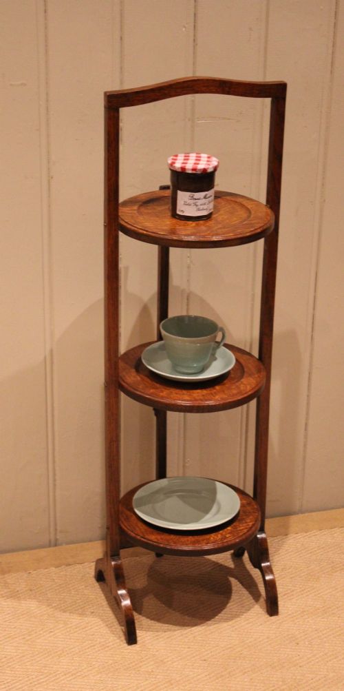 An Edwardian oak three-tier folding cake stand featuring circular recessed shelves and an arched carrying handle. View II