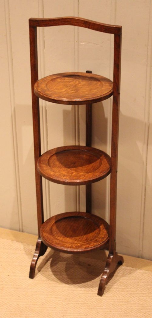An Edwardian oak three-tier folding cake stand featuring circular recessed shelves and an arched carrying handle. View III