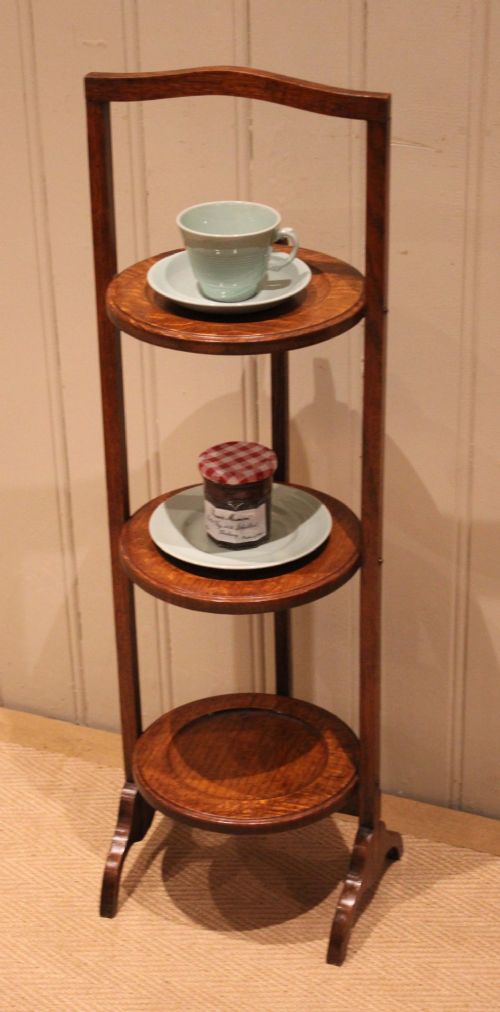 An Edwardian oak three-tier folding cake stand featuring circular recessed shelves and an arched carrying handle. View IV