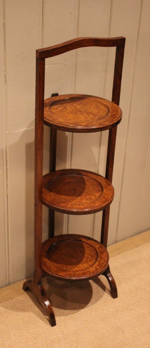 An Edwardian oak three-tier folding cake stand featuring circular recessed shelves and an arched carrying handle. View V