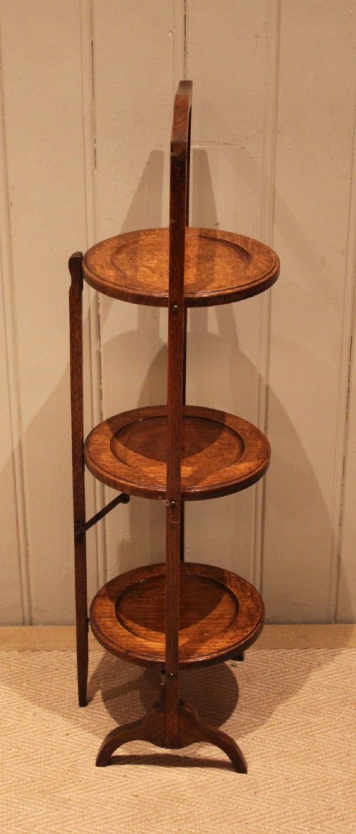 An Edwardian oak three-tier folding cake stand featuring circular recessed shelves and an arched carrying handle. View VII