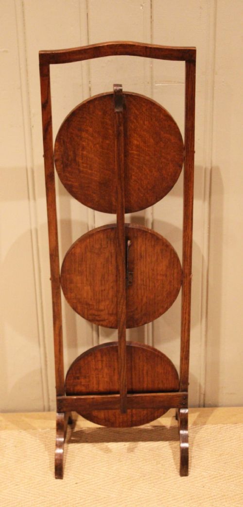 An Edwardian oak three-tier folding cake stand featuring circular recessed shelves and an arched carrying handle. View IX