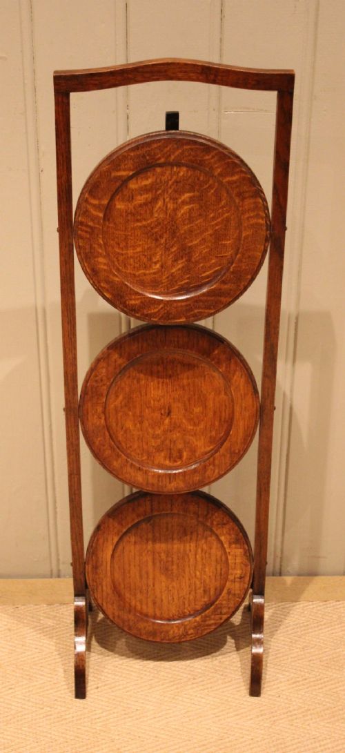 An Edwardian oak three-tier folding cake stand featuring circular recessed shelves and an arched carrying handle. View X