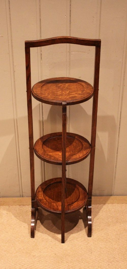 An Edwardian oak three-tier folding cake stand featuring circular recessed shelves and an arched carrying handle. View XII