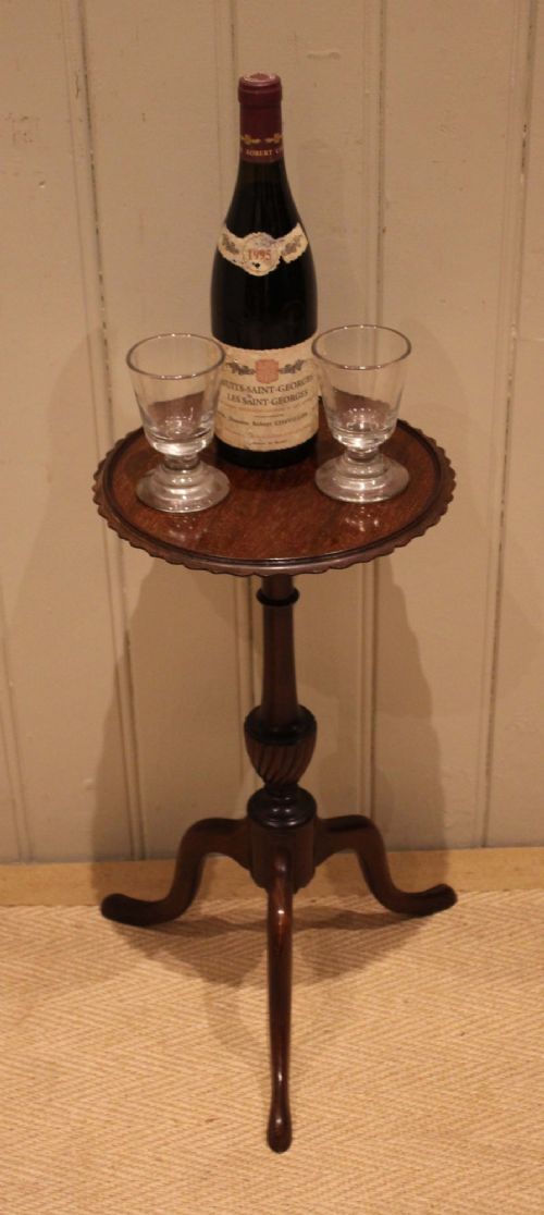 An Edwardian mahogany wine table featuring a scalloped piecrust circular top, a turned central stem, and three splayed tripod legs. View X
