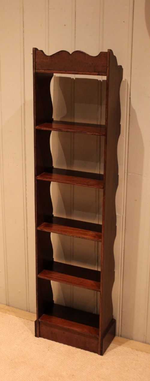 A tall and narrow dark mahogany open bookcase with five fixed shelves, shaped side aprons, and a scalloped top rail. View XII