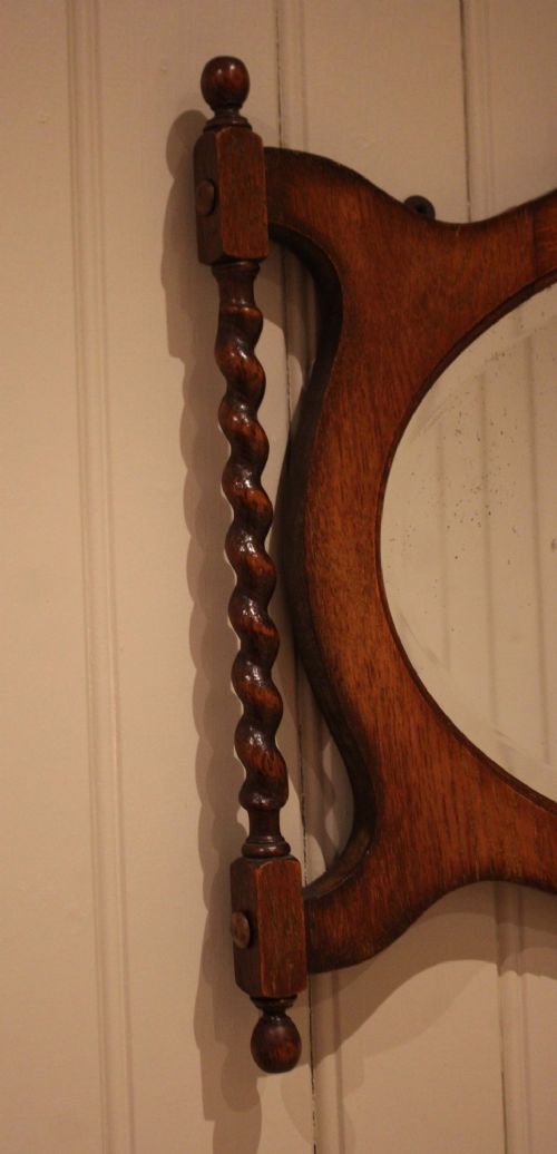 An oval glass wall mirror set within a dark carved oak frame featuring turned barley twist side pilasters and an ornate cresting. View V