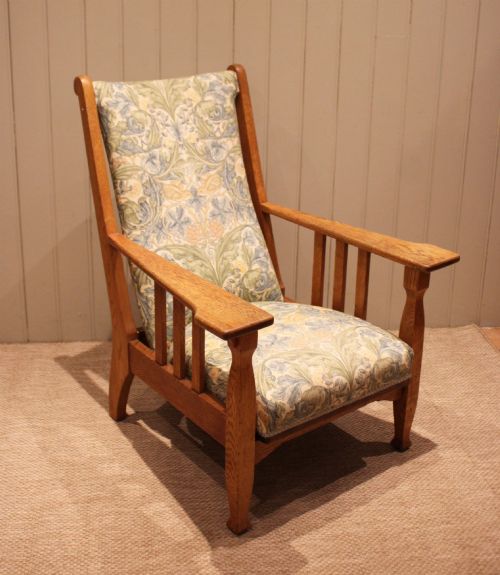 fig 1. A solid oak Arts and Crafts style armchair featuring broad flat armrests and upholstery decorated with a botanical foliage pattern.