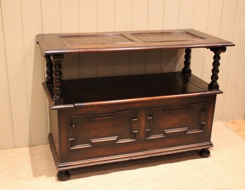 fig 1. A dark oak monks bench with geometric moulded panels on the backrest and storage base, supported by turned posts and bun feet.