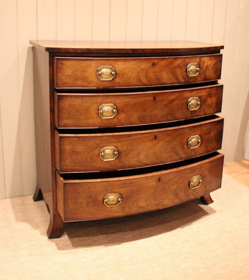 fig 1. A Georgian flame mahogany bowfront chest of drawers featuring four graduated drawers with brass handles and splayed bracket feet.
