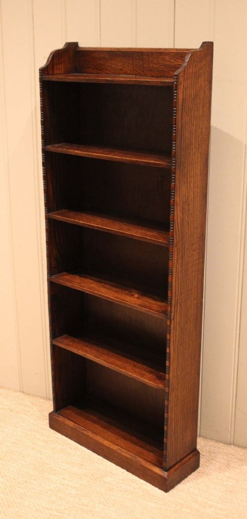 A tall, narrow dark oak open bookcase featuring five fixed shelves filled with vintage hardback books and a simple gallery top on a plinth base. View VIII