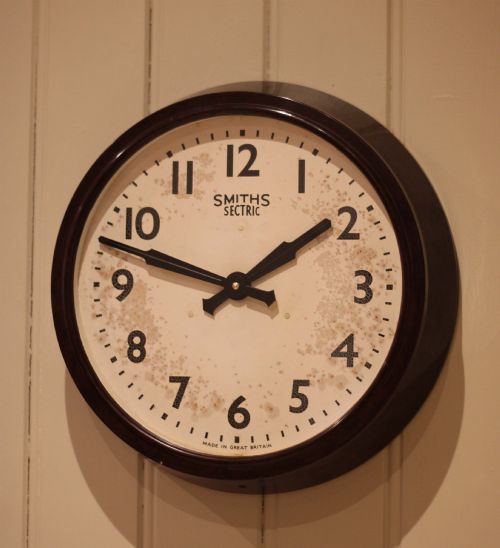 fig 1. A circular vintage British Smiths Sectric wall clock featuring a dark brown Bakelite frame and an off-white dial with black Arabic numerals.
