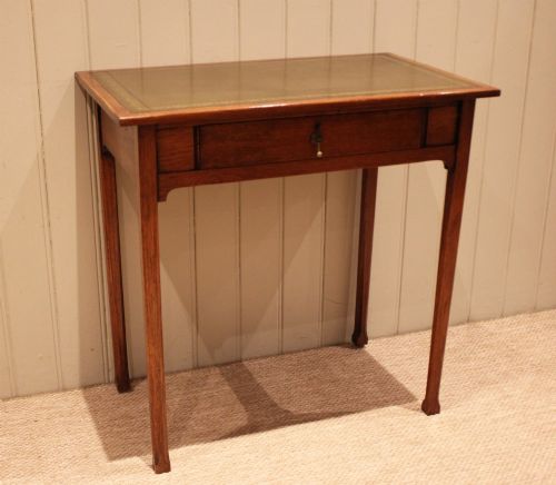 fig 1. A small rectangular Arts and Crafts oak writing desk with a green gilded leather inset top, a single frieze drawer, and tapered square legs.