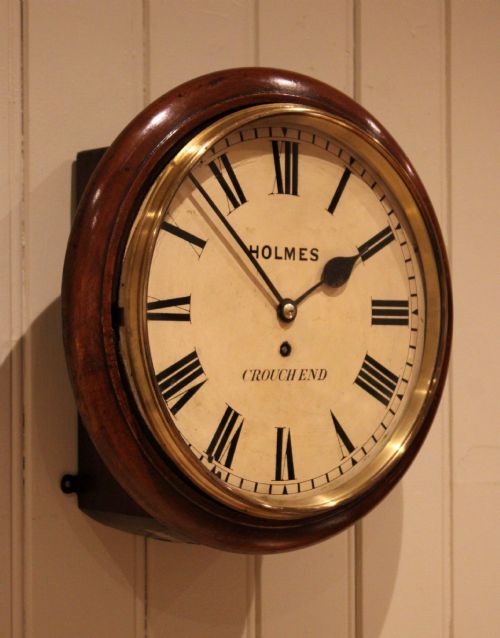 fig 1. A circular mahogany wall clock featuring a brass bezel surrounding an off-white dial with black Roman numerals.