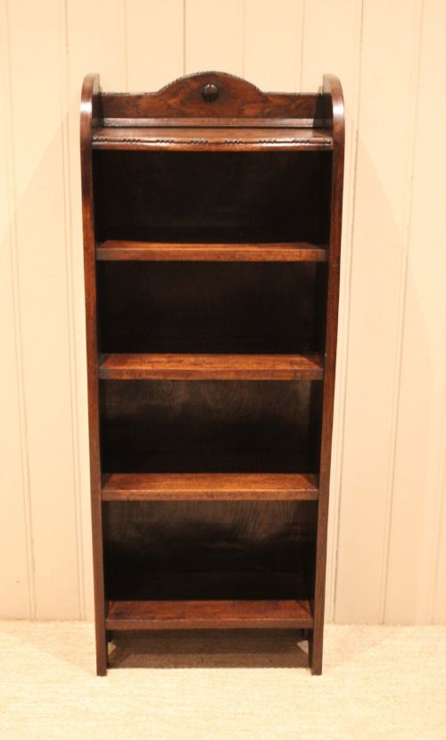 fig 1. A slim freestanding dark oak open bookcase featuring four shelves and a shaped decorative pediment with a round motif.