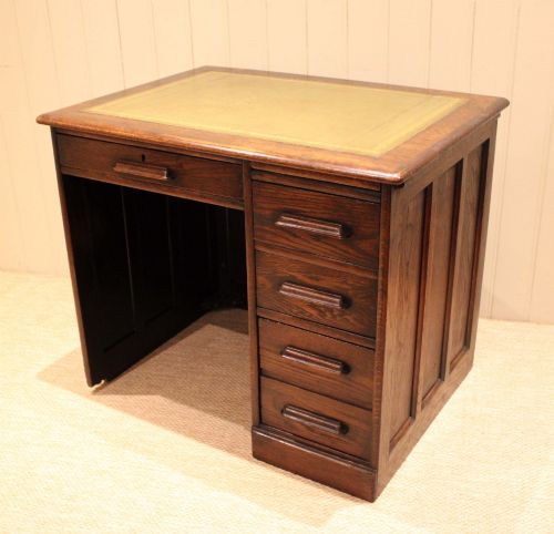 fig 1. A small solid dark oak clerks desk featuring a leather inset writing surface, a single central drawer, and a four-drawer pedestal on the right.