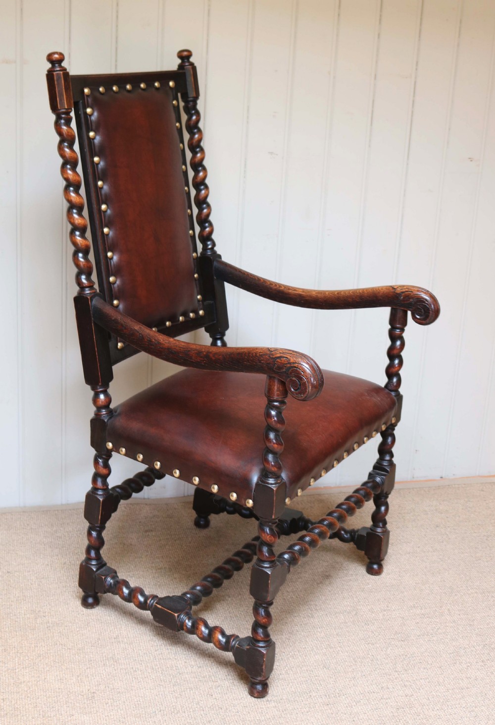 A high-backed dark oak armchair featuring barley twist columns, scroll armrests, and reddish-brown leather upholstery with brass studding. View II