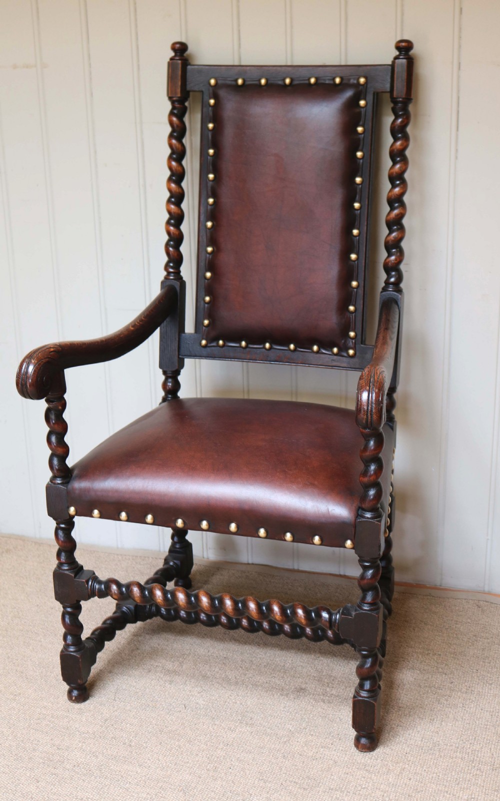 A high-backed dark oak armchair featuring barley twist columns, scroll armrests, and reddish-brown leather upholstery with brass studding. View III