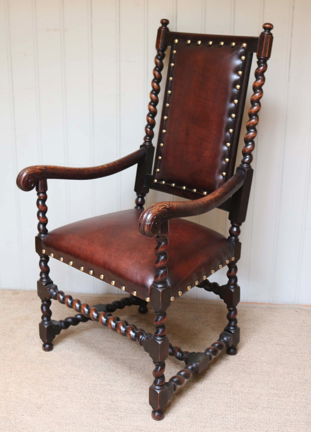 A high-backed dark oak armchair featuring barley twist columns, scroll armrests, and reddish-brown leather upholstery with brass studding. View IV