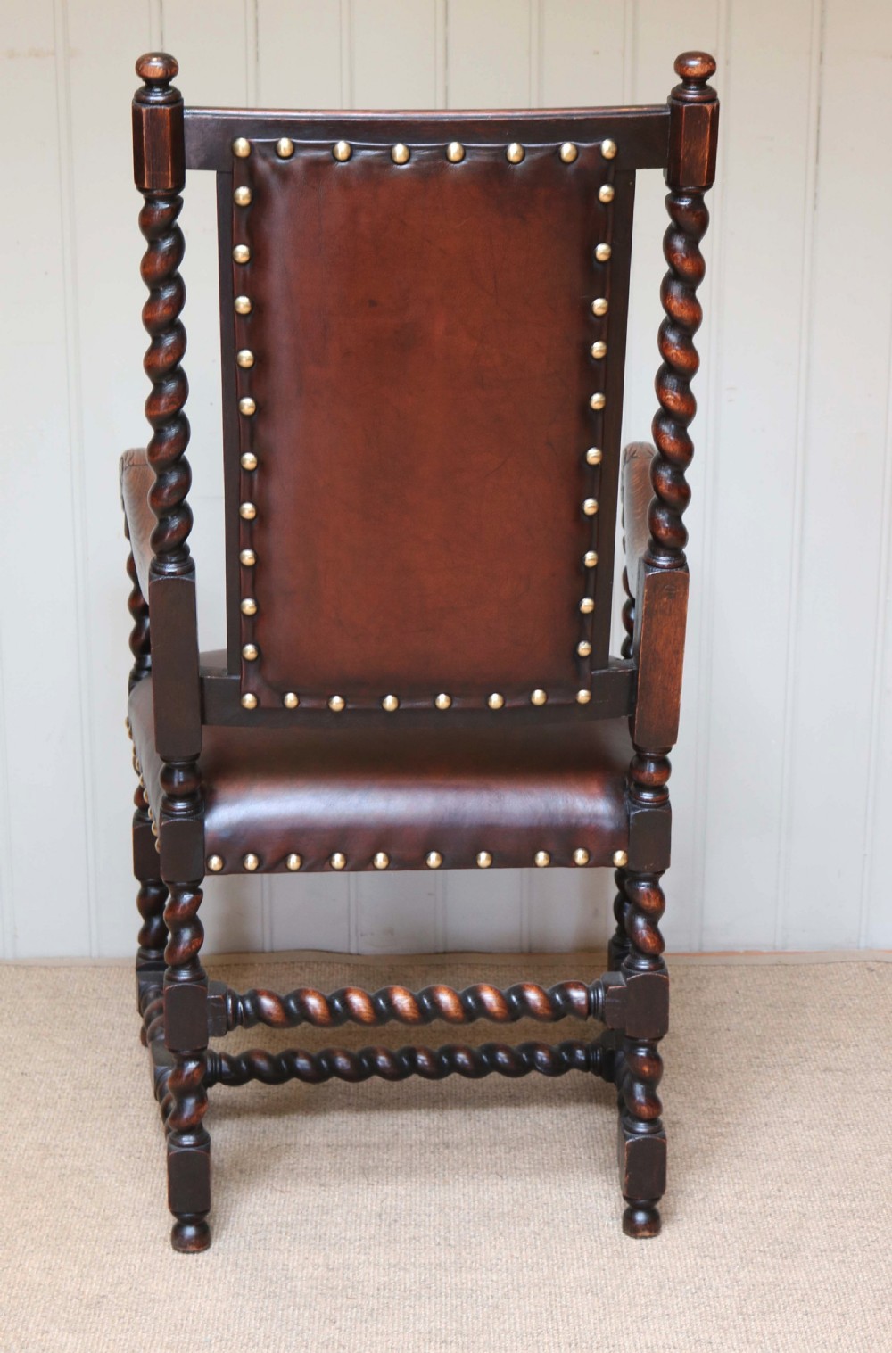 A high-backed dark oak armchair featuring barley twist columns, scroll armrests, and reddish-brown leather upholstery with brass studding. View VII