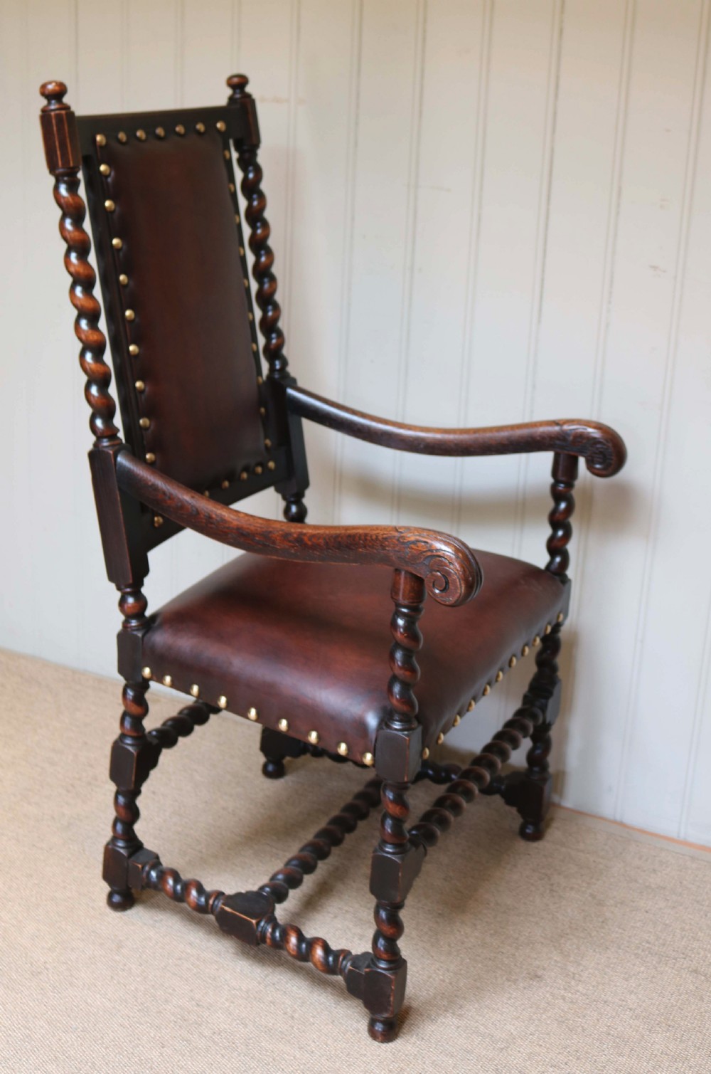 A high-backed dark oak armchair featuring barley twist columns, scroll armrests, and reddish-brown leather upholstery with brass studding. View VIII