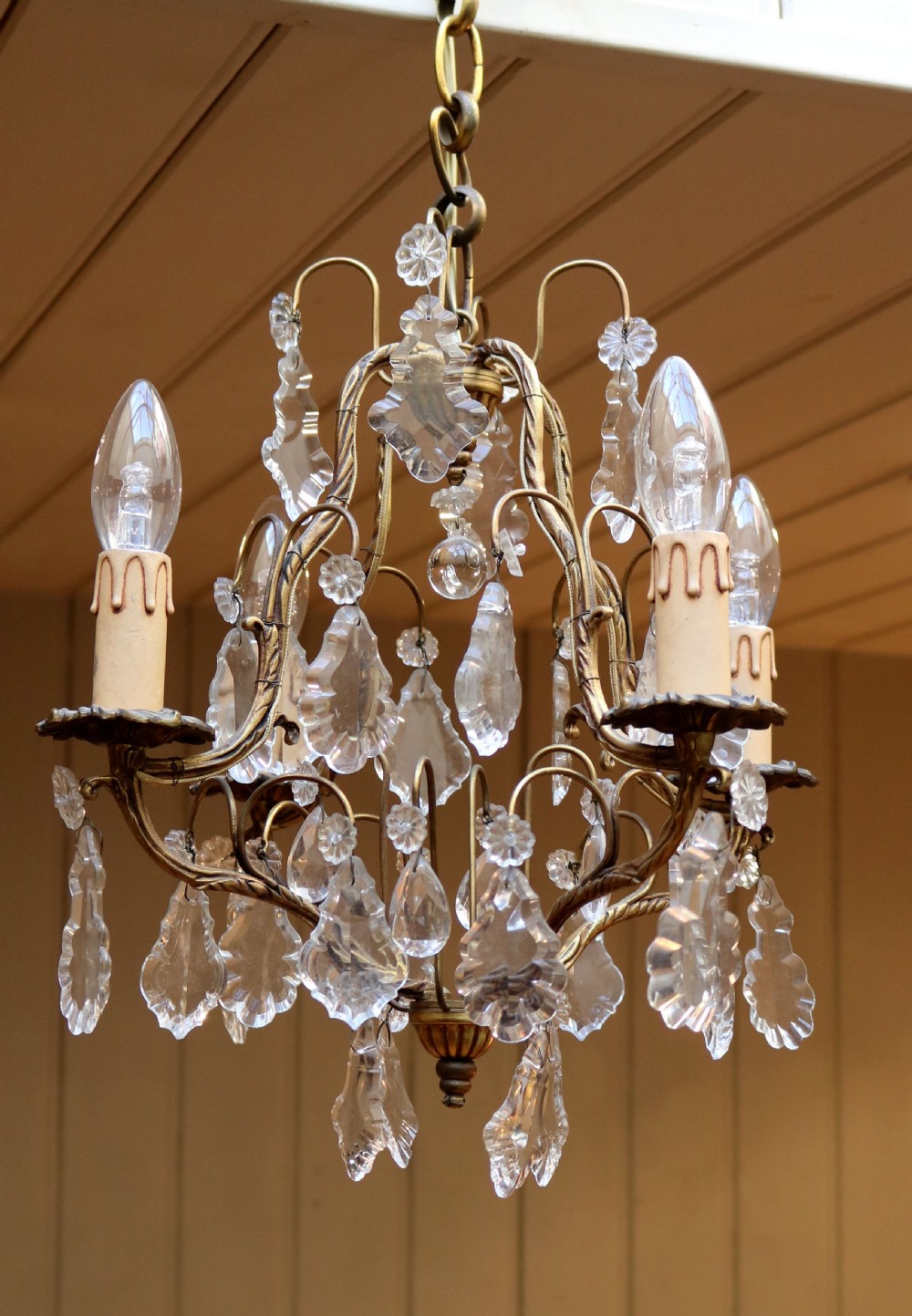 A French four-branch gilt metal chandelier adorned with clear cut glass crystal drops and faux candle sleeve light fittings.