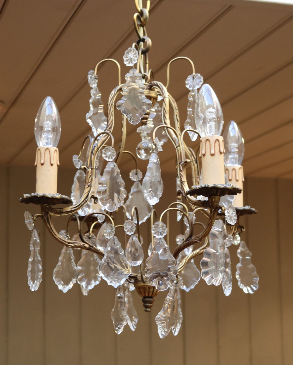 A French four-branch gilt metal chandelier adorned with clear cut glass crystal drops and faux candle sleeve light fittings. View III