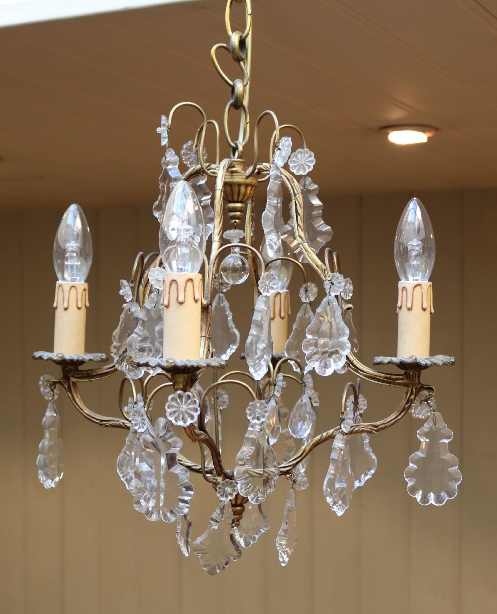 A French four-branch gilt metal chandelier adorned with clear cut glass crystal drops and faux candle sleeve light fittings. View V