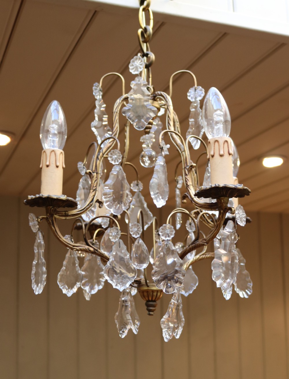 A French four-branch gilt metal chandelier adorned with clear cut glass crystal drops and faux candle sleeve light fittings. View VIII