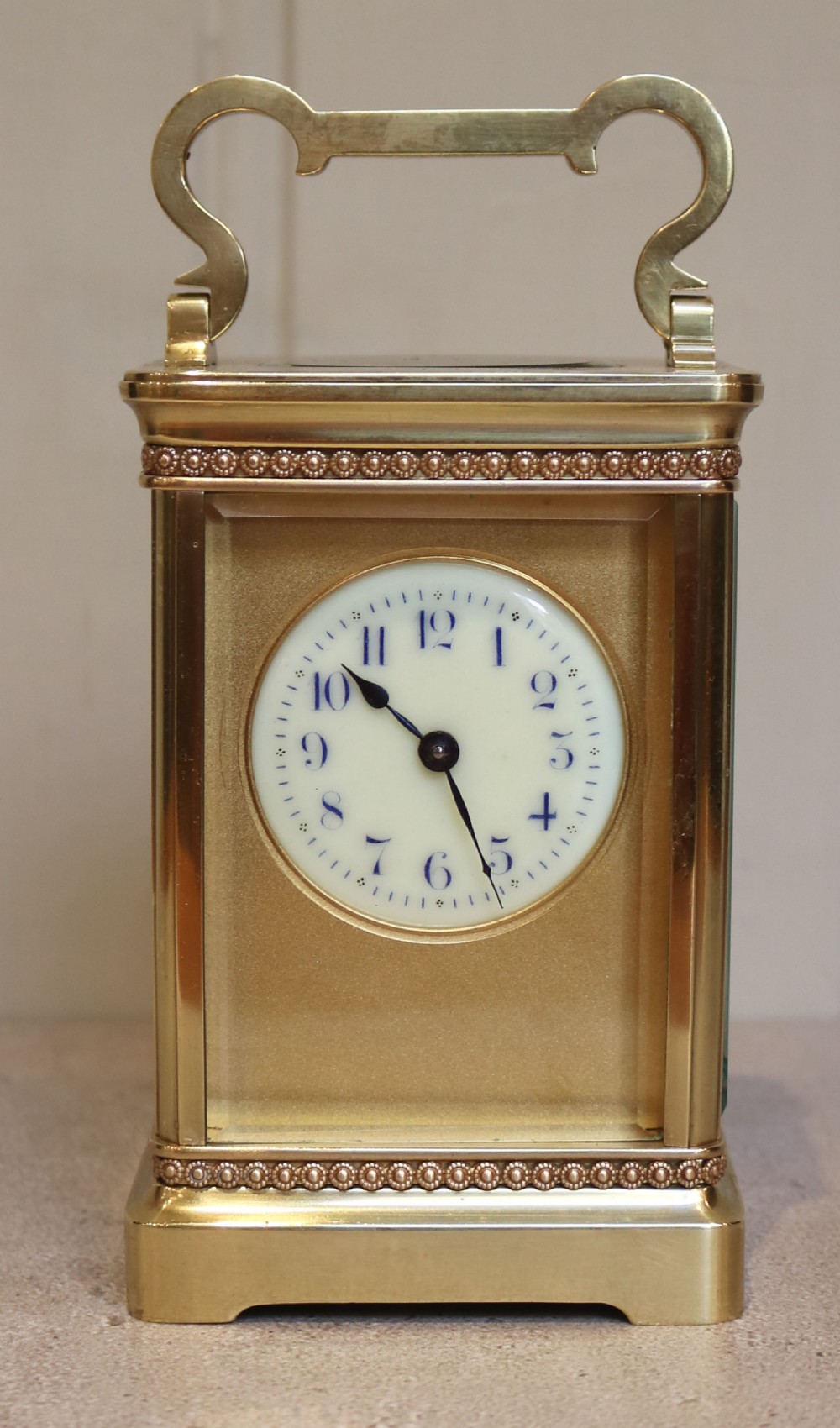 An Edwardian brass carriage clock featuring a rectangular case with glass panels, beaded trim, a top handle, and a white enamel dial with blue numerals.