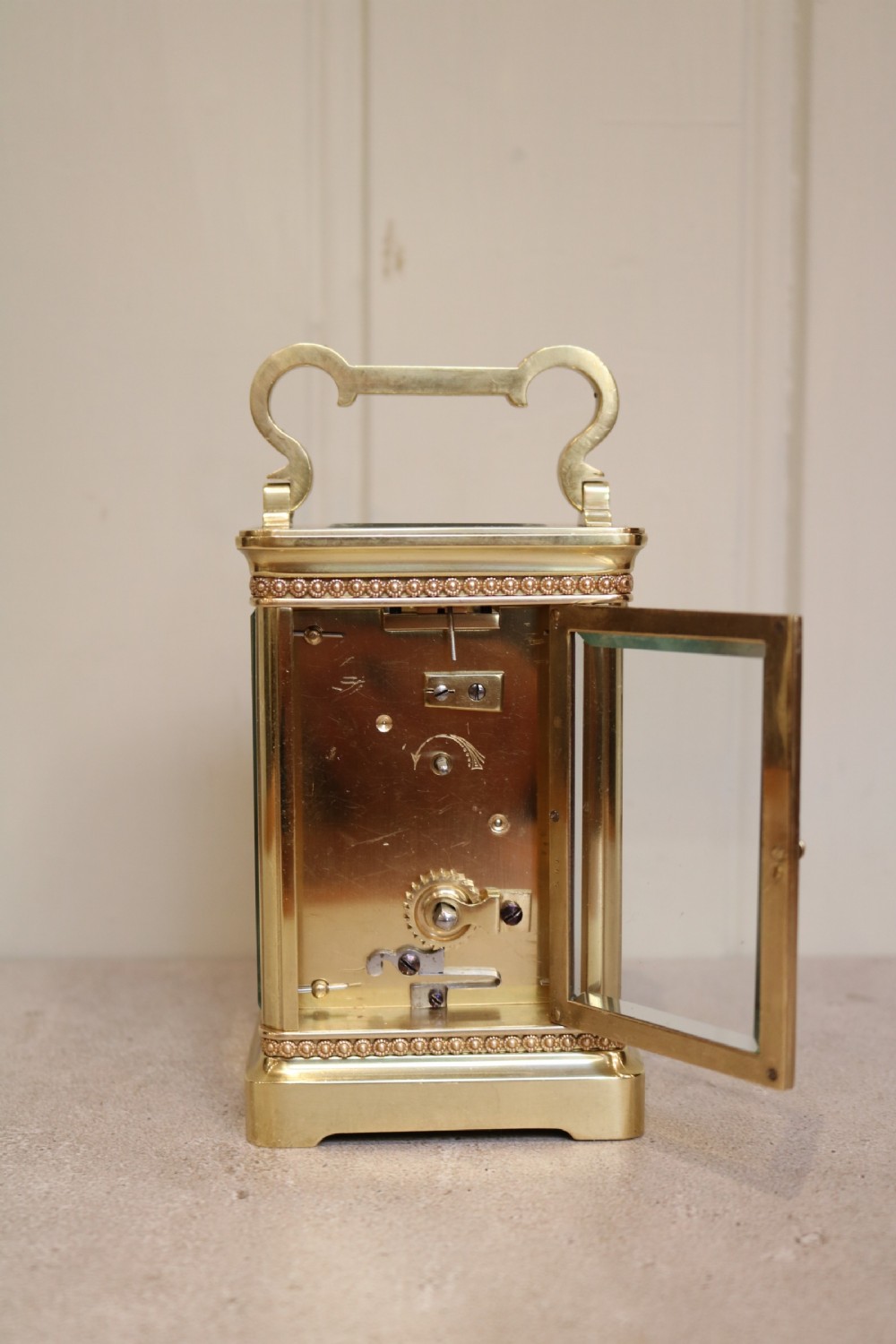 An Edwardian brass carriage clock featuring a rectangular case with glass panels, beaded trim, a top handle, and a white enamel dial with blue numerals. View VIII