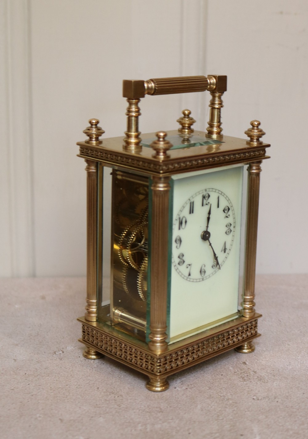 An Edwardian brass carriage clock featuring bevelled glass panels, fluted corner columns, a folding top handle, and a white dial with Arabic numerals. View II