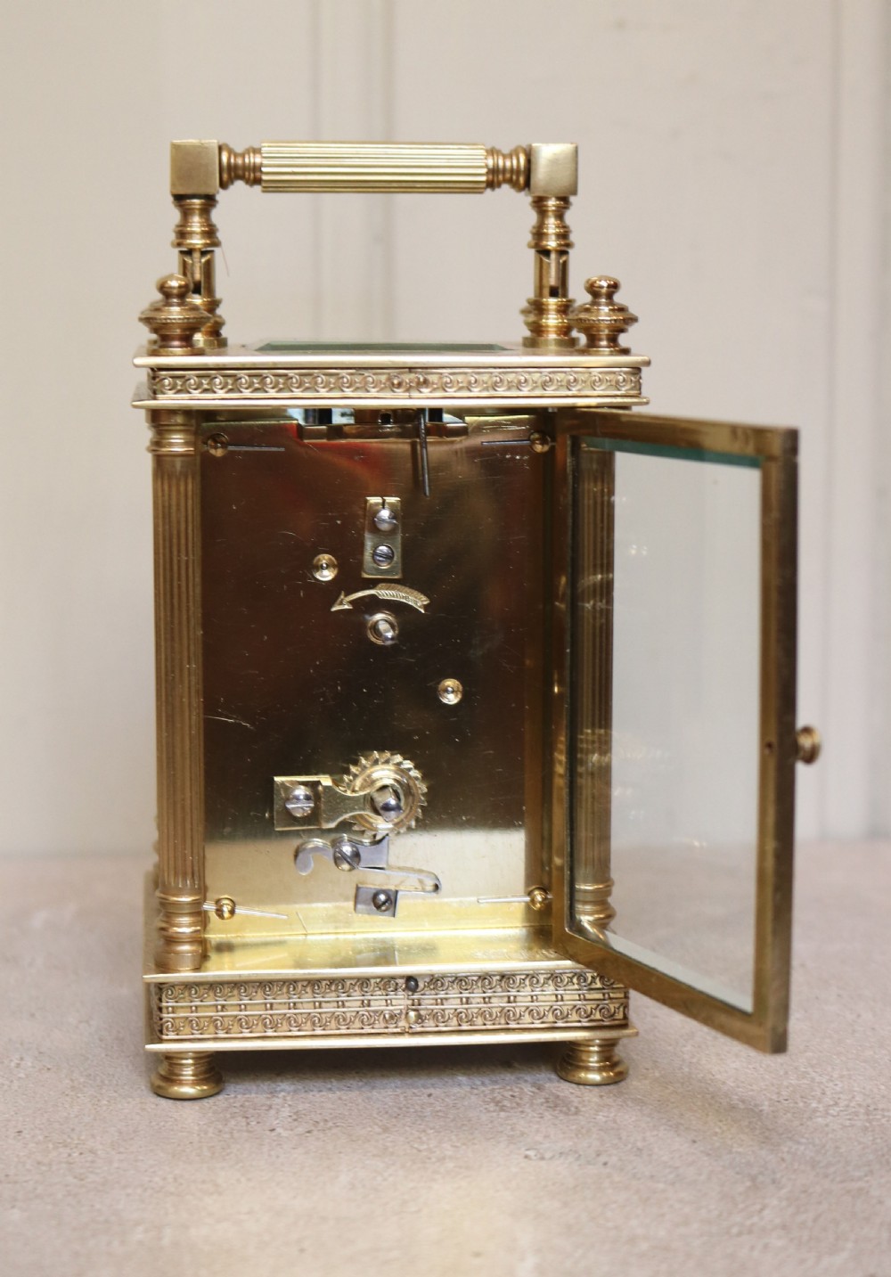 An Edwardian brass carriage clock featuring bevelled glass panels, fluted corner columns, a folding top handle, and a white dial with Arabic numerals. View VI