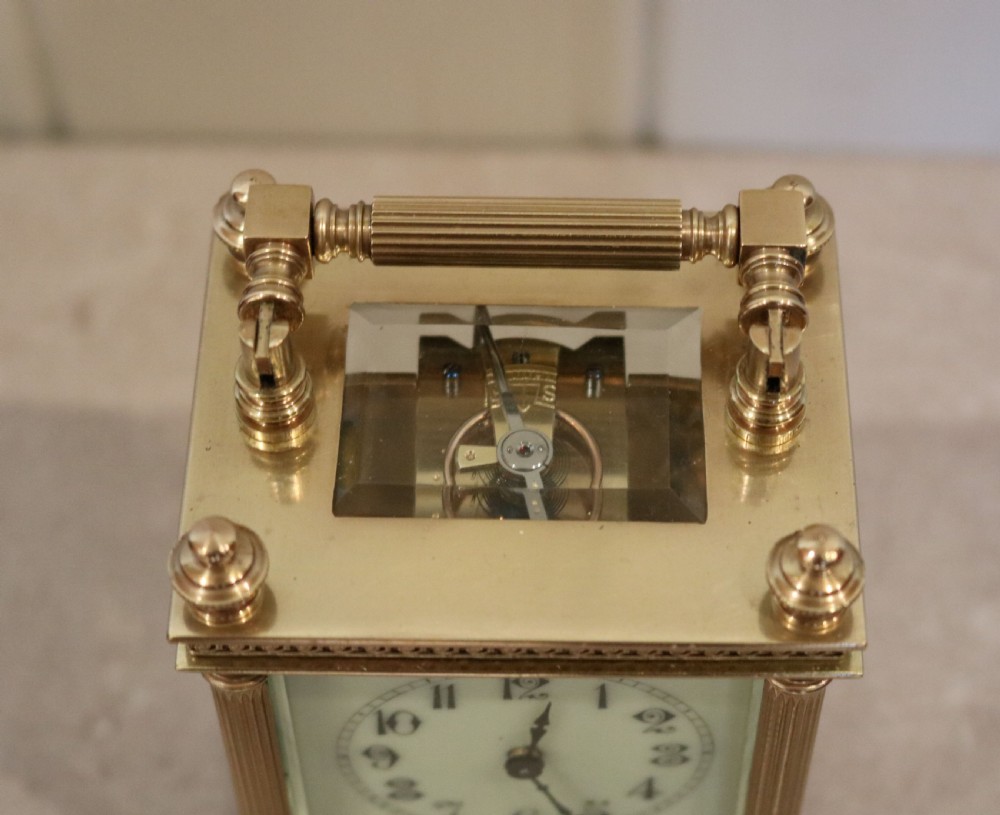 An Edwardian brass carriage clock featuring bevelled glass panels, fluted corner columns, a folding top handle, and a white dial with Arabic numerals. View IX