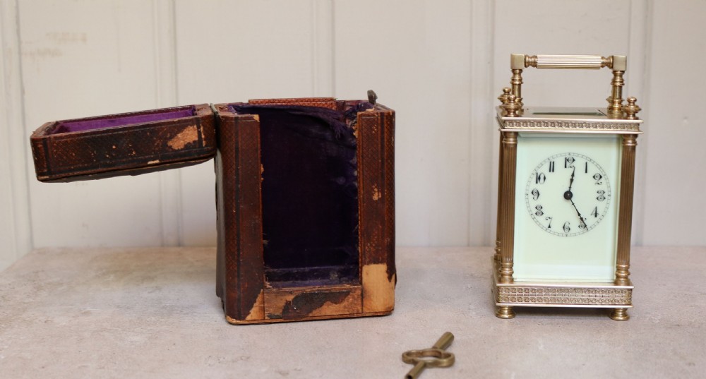 An Edwardian brass carriage clock featuring bevelled glass panels, fluted corner columns, a folding top handle, and a white dial with Arabic numerals. View X