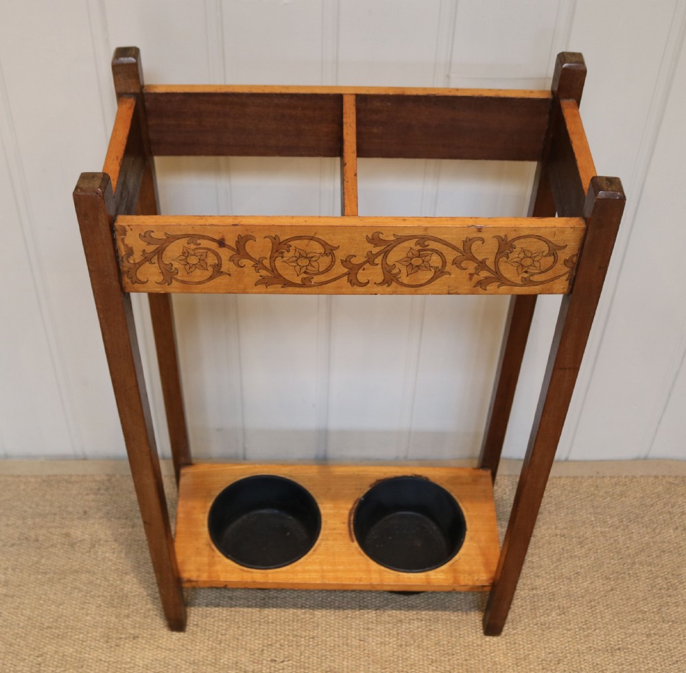 A dark wooden umbrella stand featuring a light inlaid maple top panel decorated with floral motifs, divided upper sections, and two circular black drip trays at the base. View II