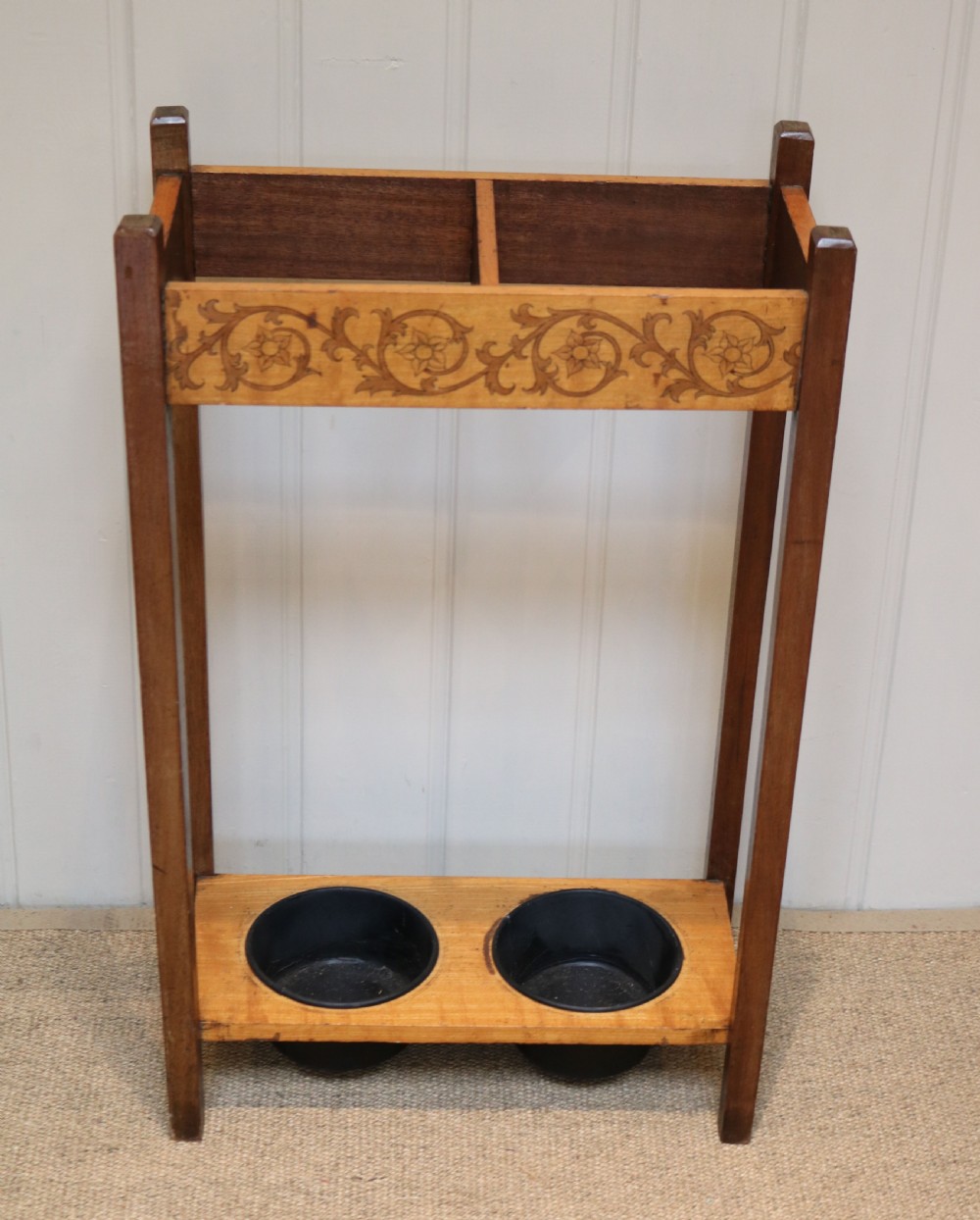 A dark wooden umbrella stand featuring a light inlaid maple top panel decorated with floral motifs, divided upper sections, and two circular black drip trays at the base. View IV