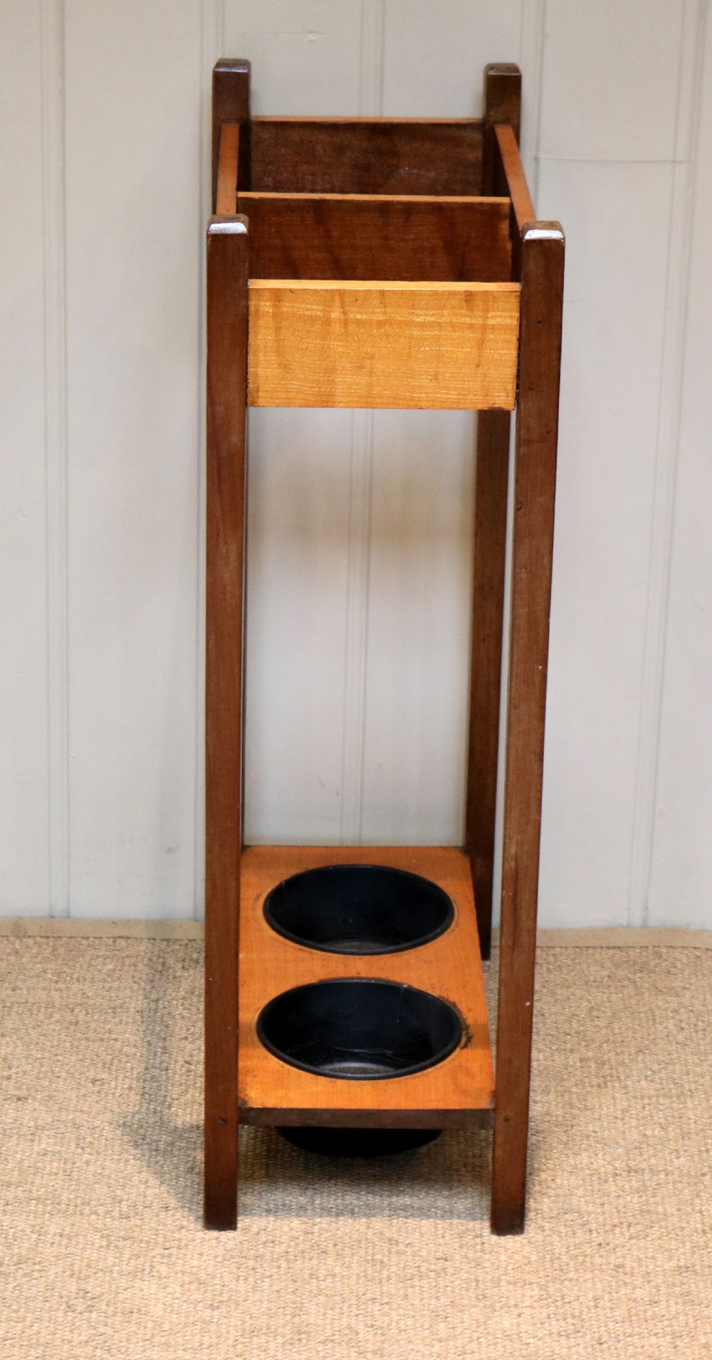 A dark wooden umbrella stand featuring a light inlaid maple top panel decorated with floral motifs, divided upper sections, and two circular black drip trays at the base. View VI