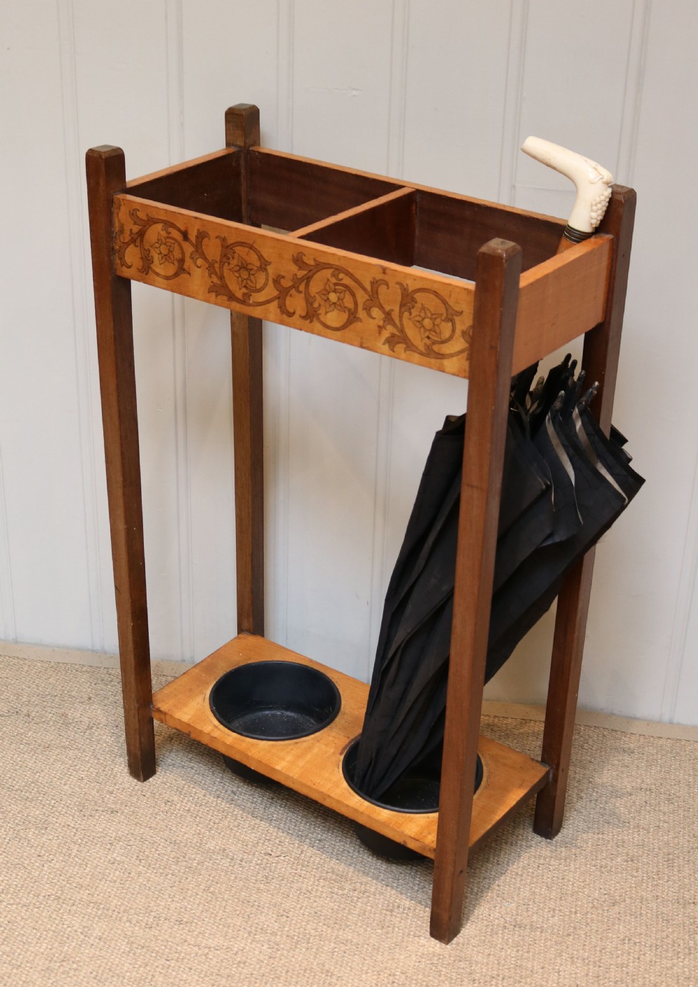 A dark wooden umbrella stand featuring a light inlaid maple top panel decorated with floral motifs, divided upper sections, and two circular black drip trays at the base. View VII