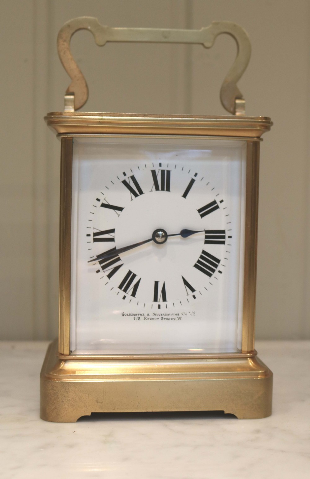 A large rectangular brass carriage clock featuring bevelled glass side panels, a white enamel dial with black Roman numerals, and a hinged top handle.
