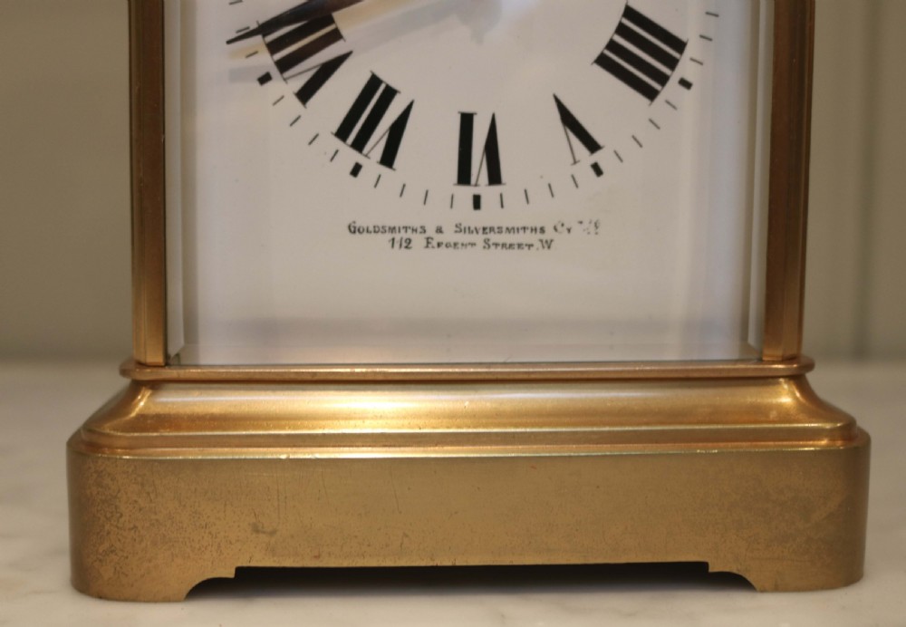 A large rectangular brass carriage clock featuring bevelled glass side panels, a white enamel dial with black Roman numerals, and a hinged top handle. View II
