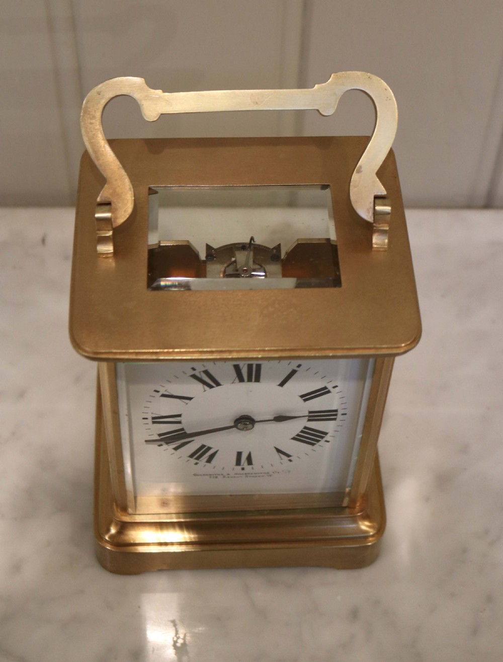 A large rectangular brass carriage clock featuring bevelled glass side panels, a white enamel dial with black Roman numerals, and a hinged top handle. View III