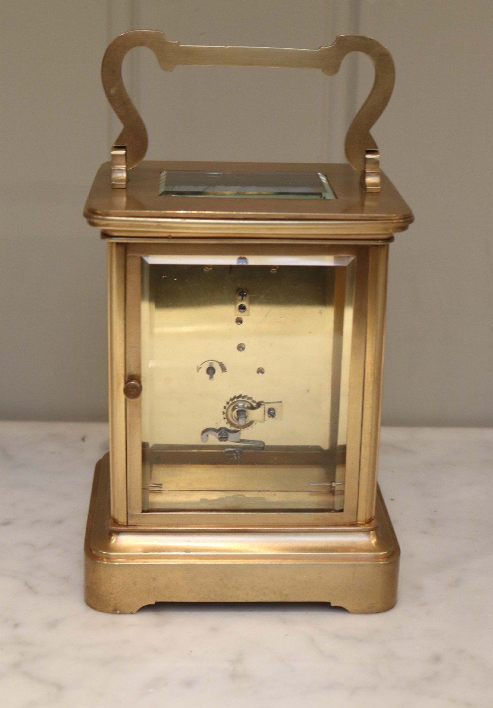 A large rectangular brass carriage clock featuring bevelled glass side panels, a white enamel dial with black Roman numerals, and a hinged top handle. View V