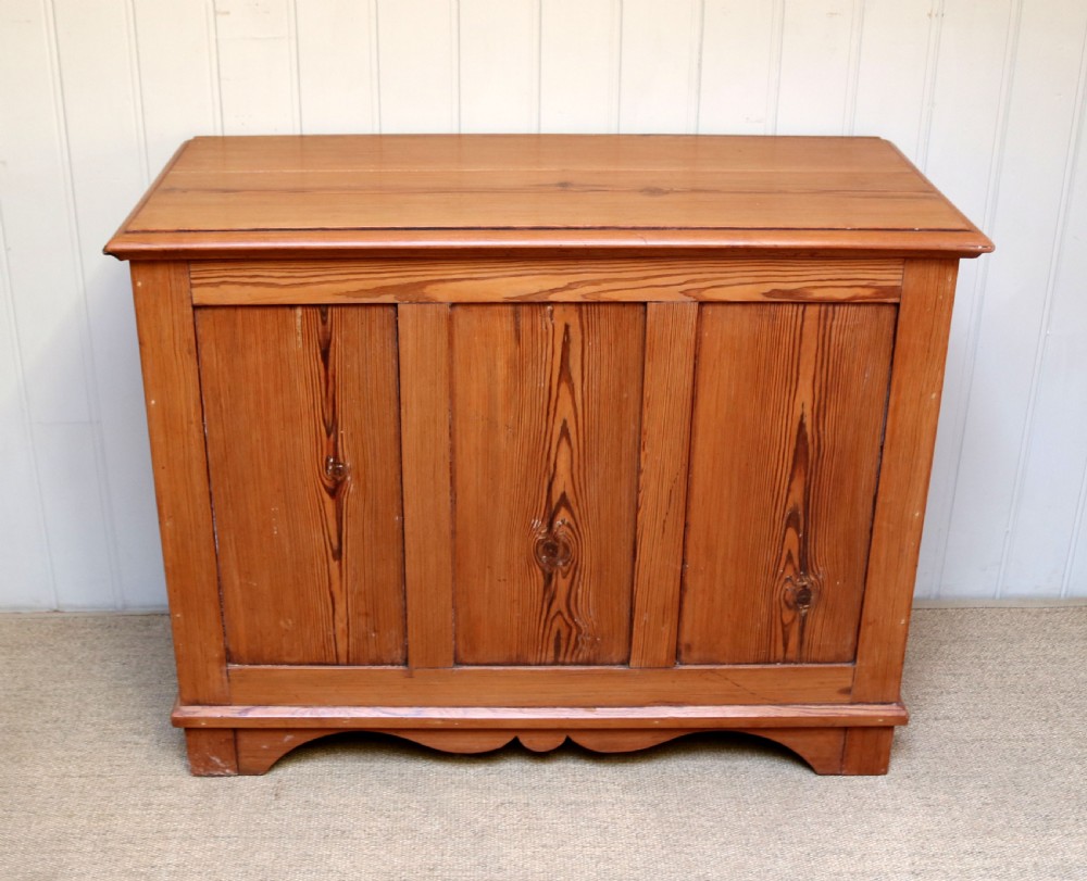 A rectangular warm pine storage box featuring three panelled front sections, a flat hinged top, and a shaped plinth base. View II