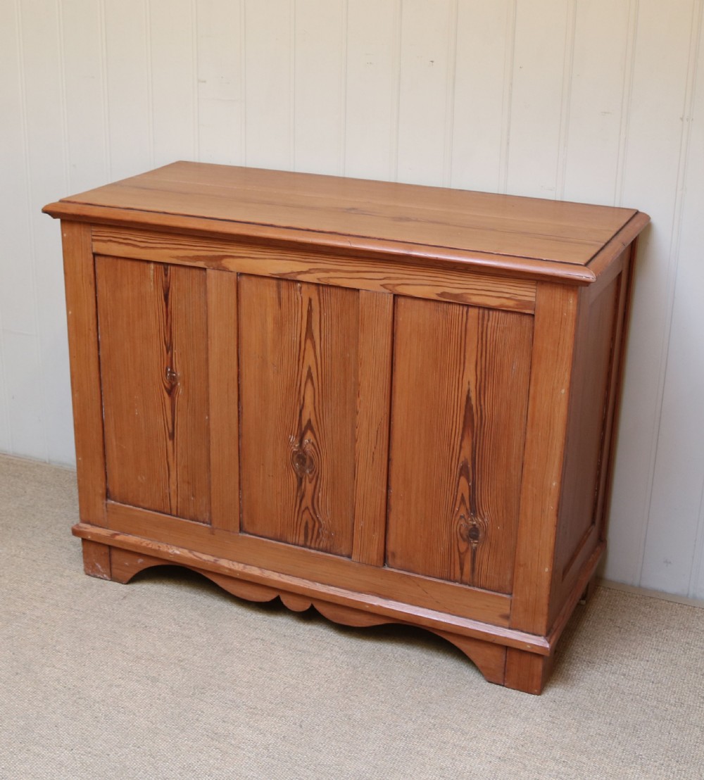 A rectangular warm pine storage box featuring three panelled front sections, a flat hinged top, and a shaped plinth base. View III